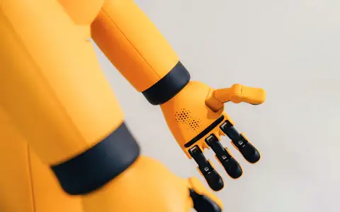 Yellow robotic arm with a mechanical hand, evoking AI agents that make payments autonomously