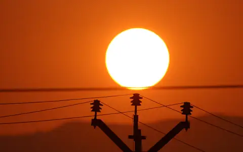 Sun setting behind electricity power lines in India, evoking household utility bills for NRIs