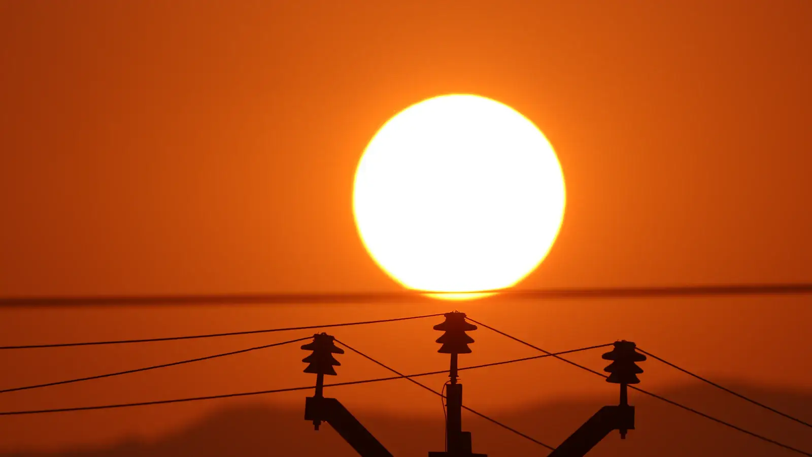 Sun setting behind electricity power lines in India, evoking household utility bills for NRIs