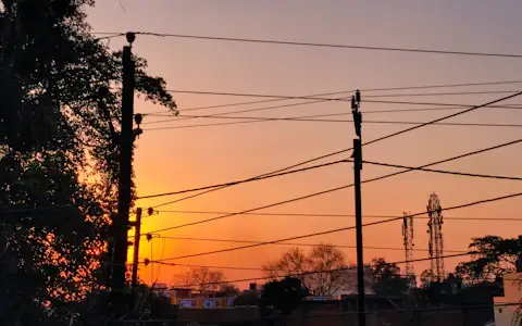 Warm sunset glowing behind power lines and poles in Chhattisgarh, India, household electricity supply