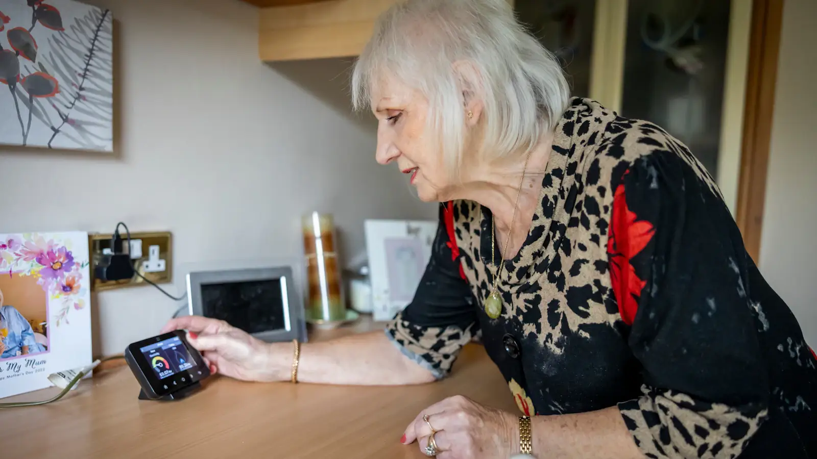Older woman sitting at a table looking at her phone, staying in touch with family