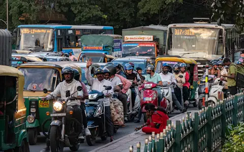 Busy Bangalore street with buses and scooters under green trees, where traffic e-challans apply