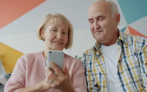 Elderly couple at home looking together at a smartphone, receiving money sent from abroad
