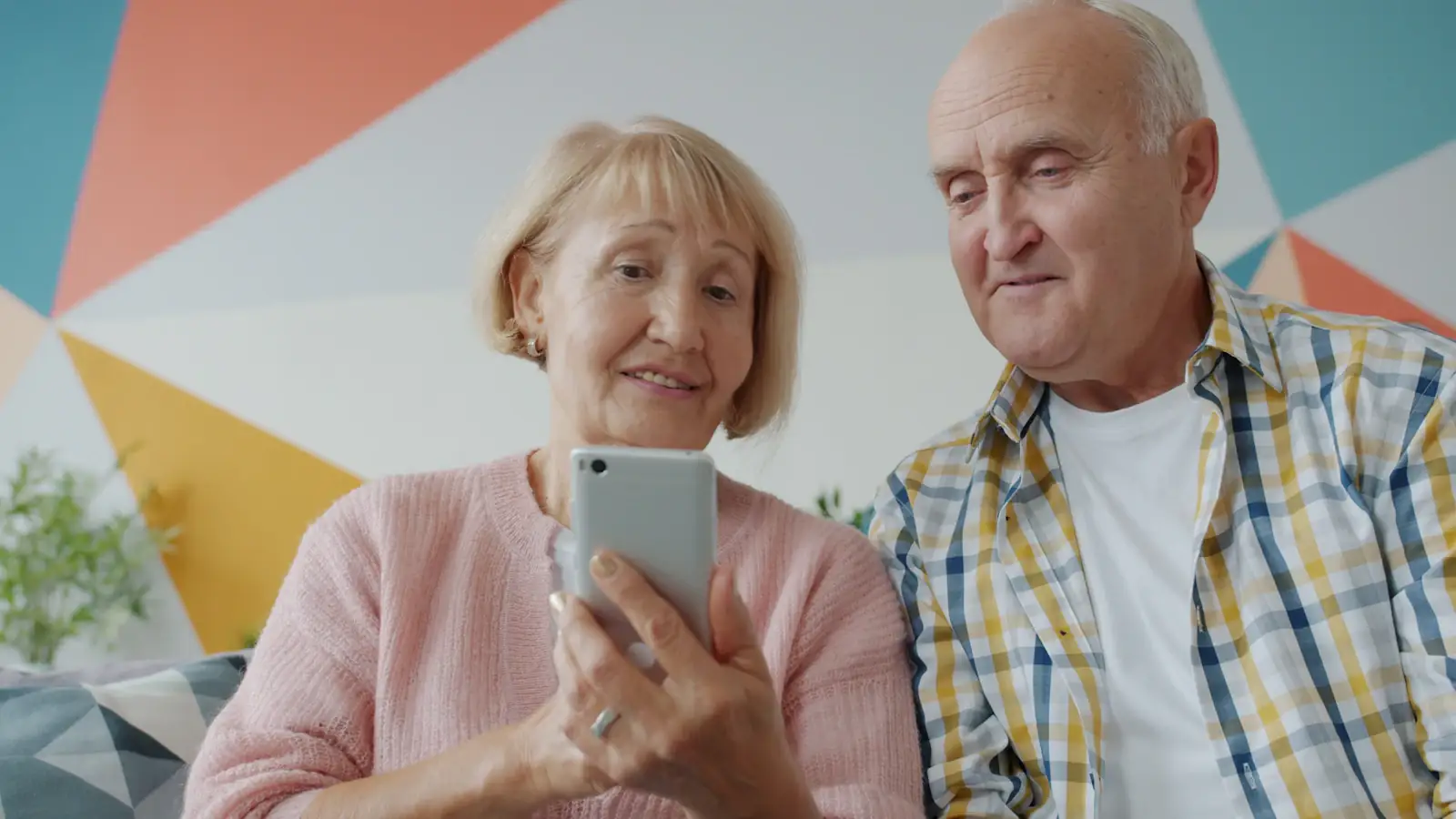 Elderly couple at home looking together at a smartphone, receiving money sent from abroad