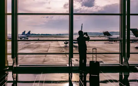 Silhouetted traveller photographing a plane through airport glass, evoking cross-border payment flows