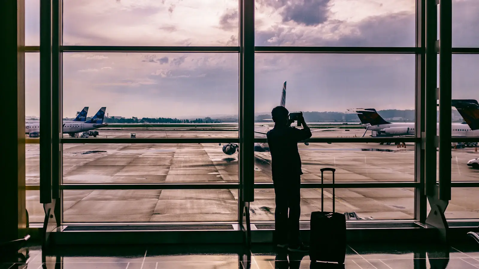 Silhouetted traveller photographing a plane through airport glass, evoking cross-border payment flows