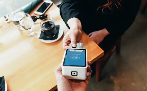 Hand holding a card payment terminal, showing how crypto and stablecoin cards are accepted