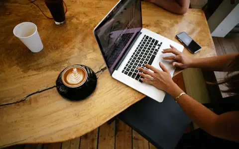 Overhead view of a freelancer working on a laptop at a wooden cafe table with coffee
