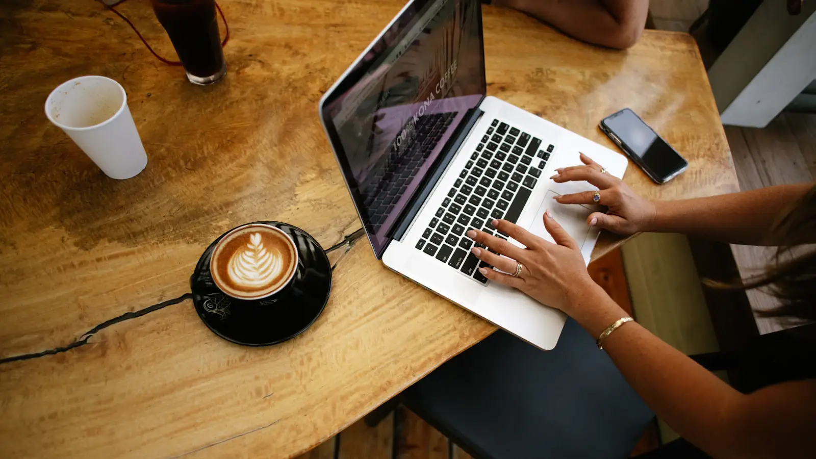 Overhead view of a freelancer working on a laptop at a wooden cafe table with coffee