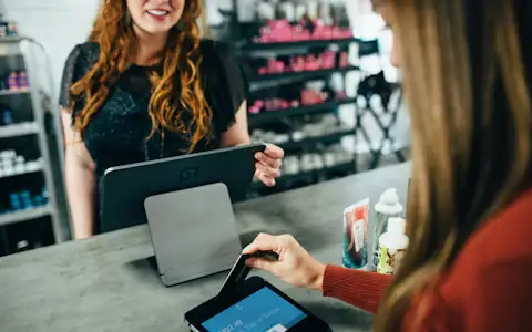 Woman holding a payment card at a shop counter, ready to pay with a crypto card