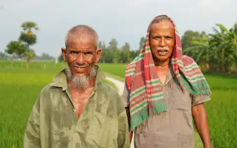 Two smiling farmers standing in a green field in rural Bangladesh