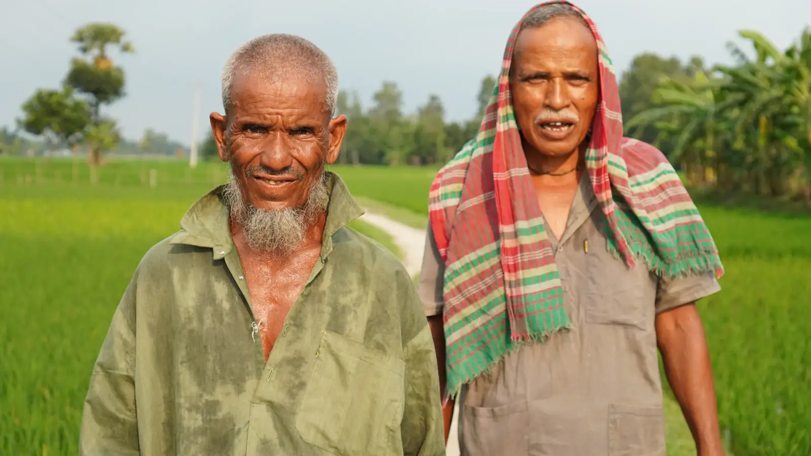 Two smiling farmers standing in a green field in rural Bangladesh