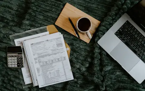 Laptop, household bills, calculator and coffee spread out for monthly budgeting