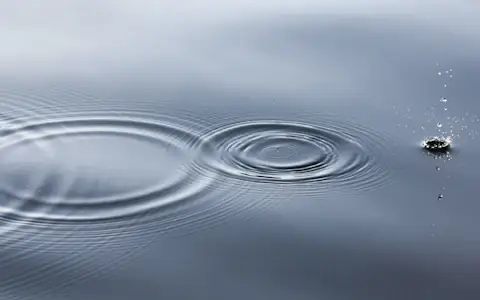 Water droplet sending ripples across a calm sea surface