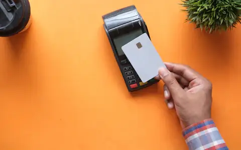 Hand holding a blank payment card near a card terminal on an orange background