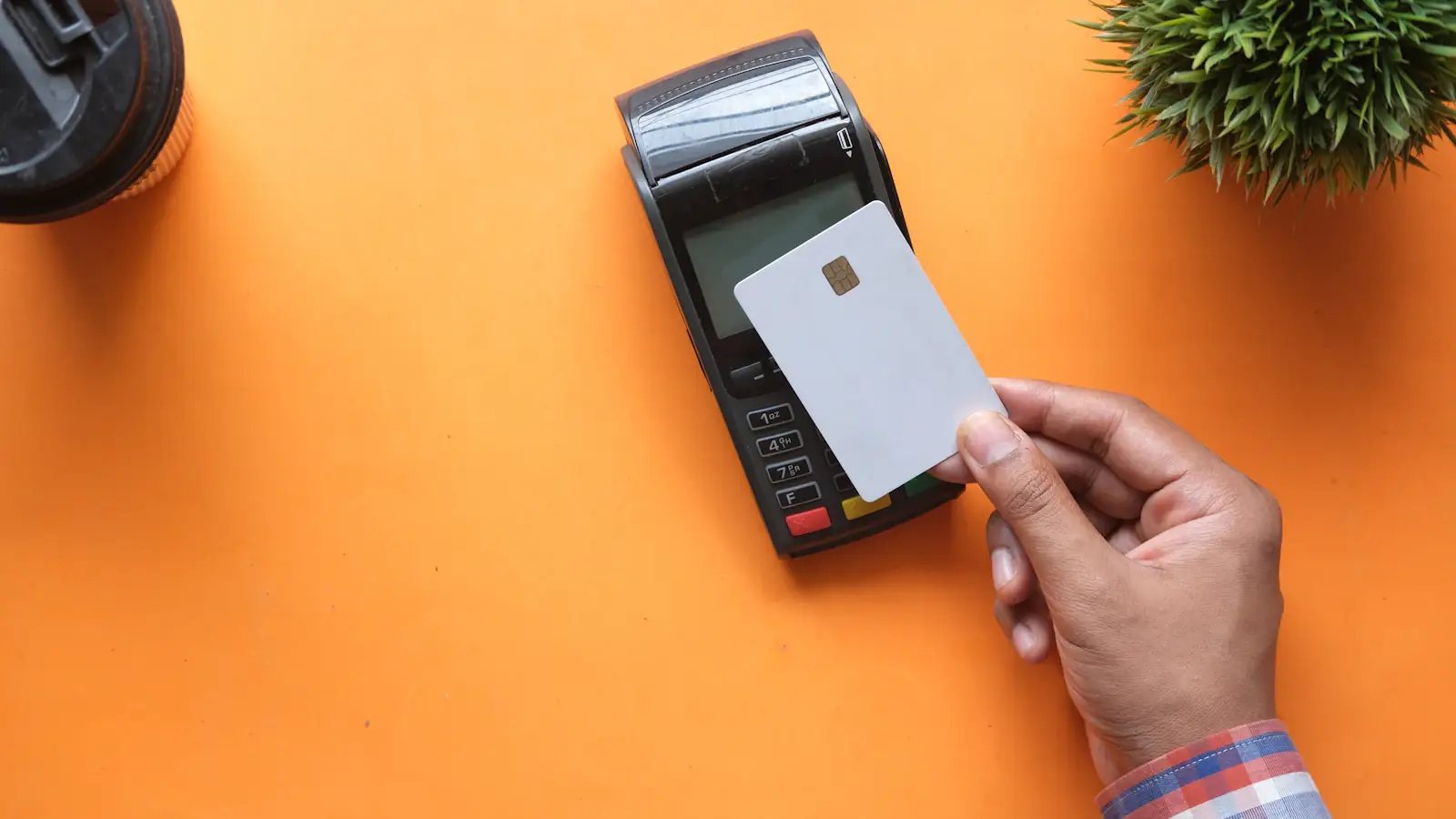 Hand holding a blank payment card near a card terminal on an orange background