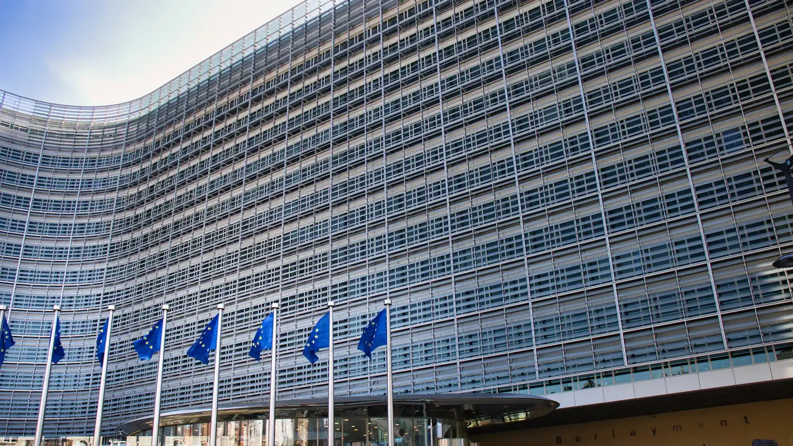 European Union flags flying outside a modern glass building, symbol of EU regulation