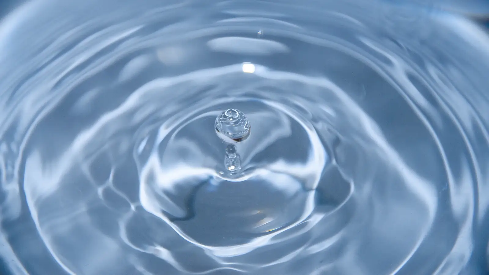 Single blue water droplet making a circular ripple, a small shock spreading outward