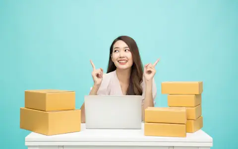 Small business owner working on a laptop surrounded by shipping boxes, managing business payments