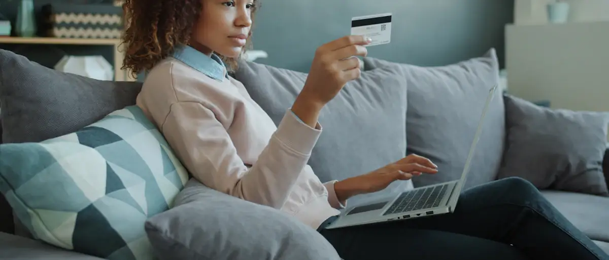 Woman on a sofa paying bills online with a credit card and laptop at home