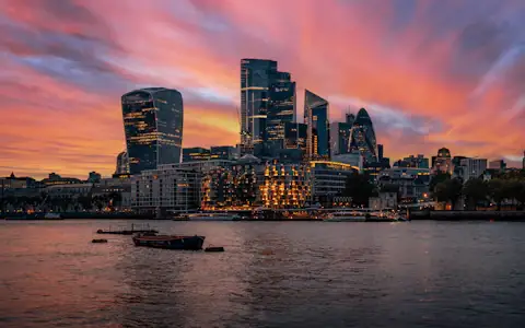 Sunset over Bishopsgate towers in the City of London with boats on the river