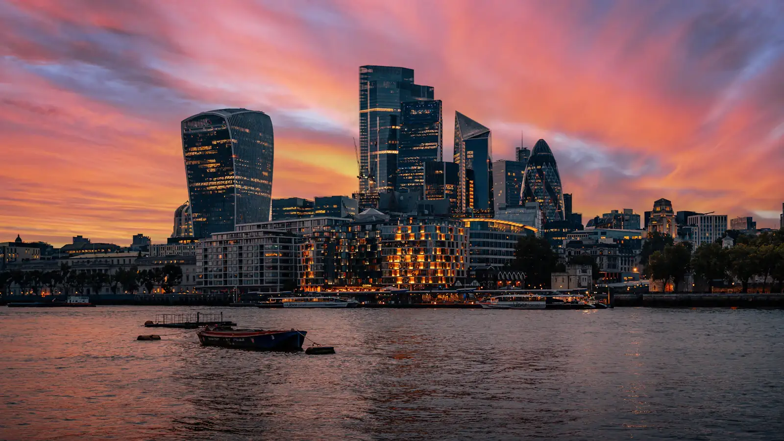 Sunset over Bishopsgate towers in the City of London with boats on the river