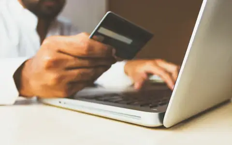 Person at a laptop holding a payment card, paying a supplier invoice online with a virtual card
