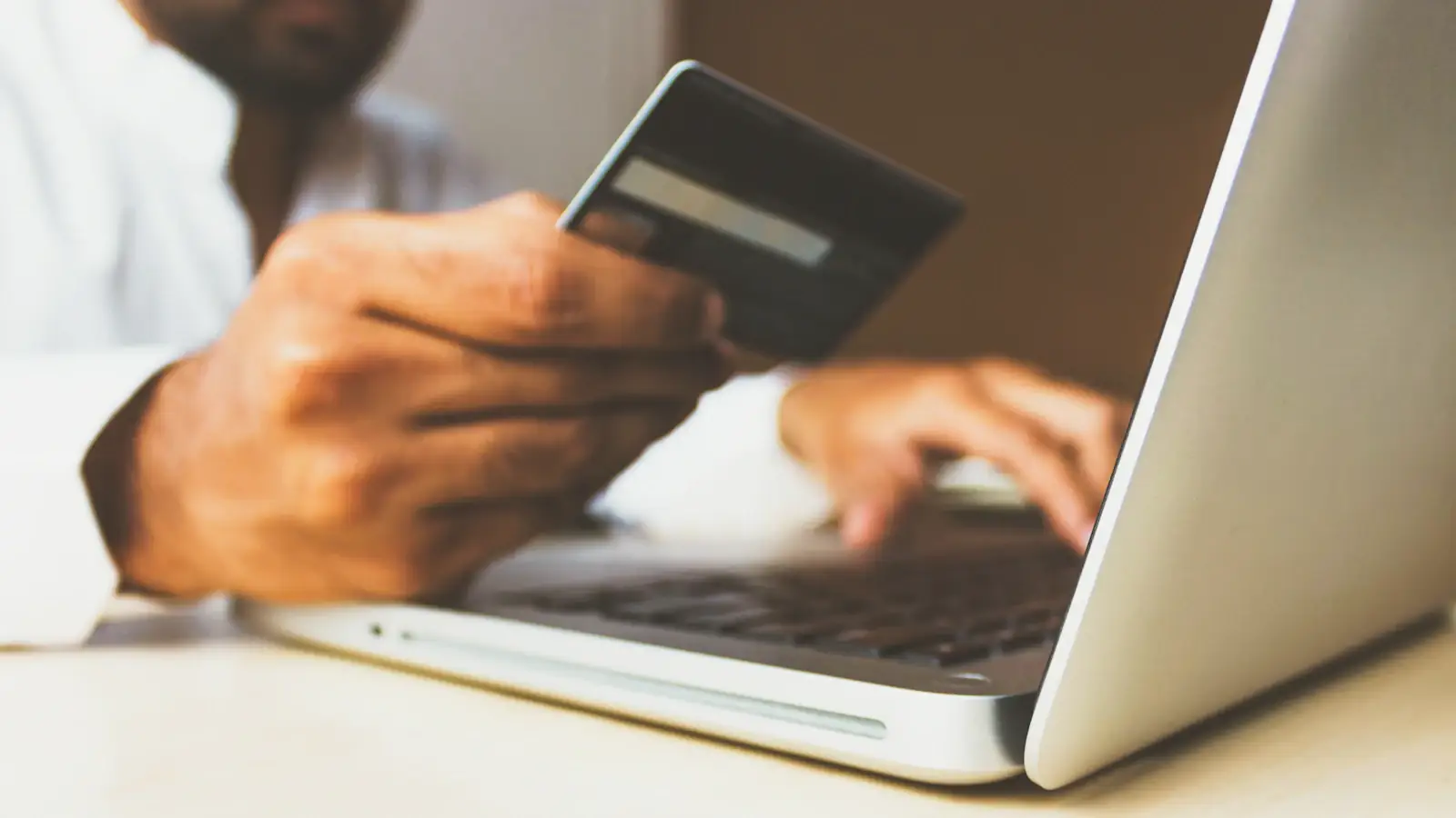 Person at a laptop holding a payment card, paying a supplier invoice online with a virtual card
