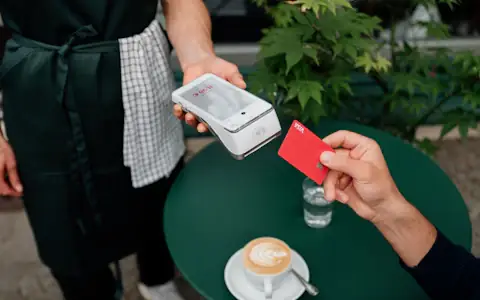 Customer tapping a Visa card on a payment terminal at a cafe table, a card network settlement in action
